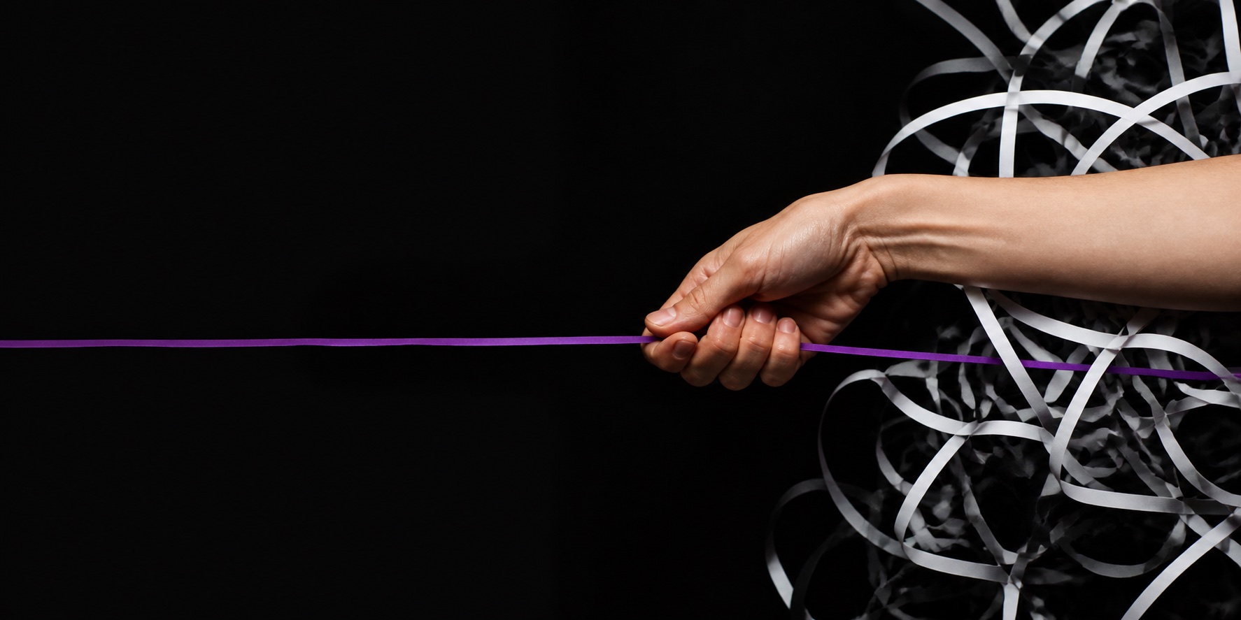 A hand pulling one violet thread from a tangle of white ribbons